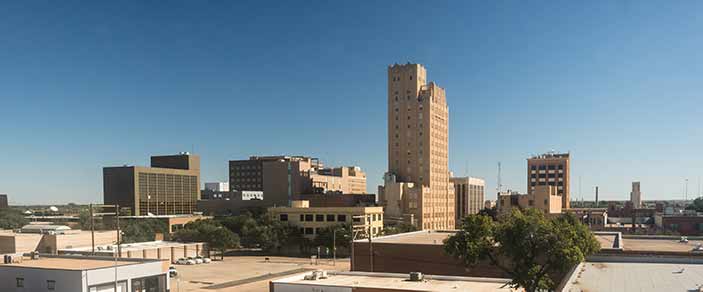 Downtown city skyline with tall beige tower and mid-rise buildings under clear blue sky