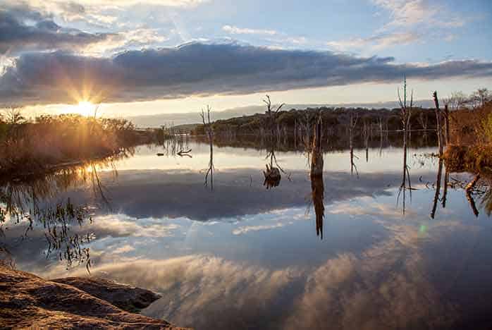Sunset over flooded wetland with dead trees reflecting in still water
