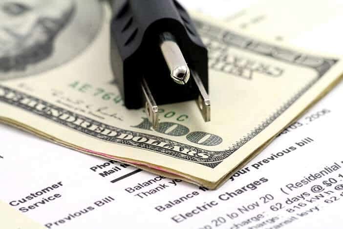 Electric plug on hundred dollar bills with utility bill showing balance and electric charges