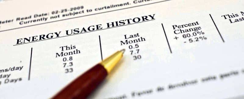Energy usage history document showing monthly consumption data with pen pointing to figures